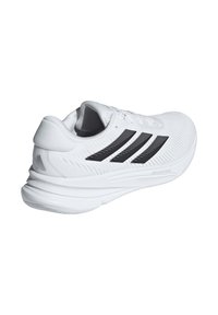 Chaussure de sport blanche avec une tige en tricot texturé, présentant trois bandes noires, un talon rembourré et une semelle profilée pour le soutien.