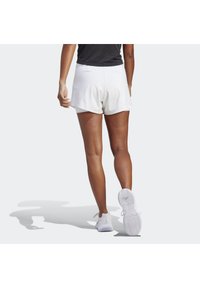 Pantalones cortos deportivos blancos con una textura suave y un ajuste holgado, combinados con una camiseta negra y zapatillas blancas. Vista desde la espalda.