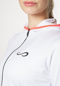 Vit zip-up hoodie med strukturerad tyg, svart logotyp på bröstet och kontrasterande orange detaljer på huvan och dragkedjan.