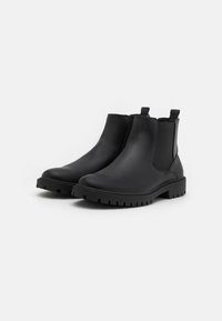 Bottines Chelsea noires en cuir lisse avec des panneaux latéraux élastiques et des tirants. Elles présentent une semelle en caoutchouc robuste et texturée.