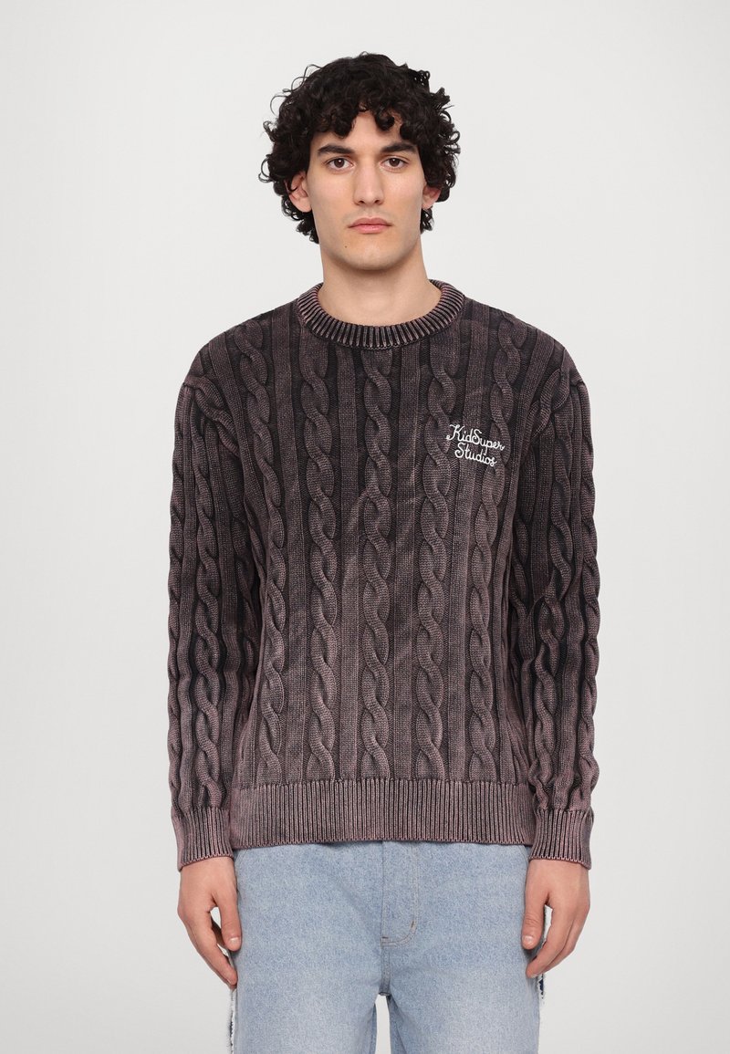 Pull en tricot câblé gris foncé avec un col rond, des poignets et un ourlet côtelés ; présente un logo brodé discret sur la poitrine gauche.