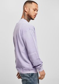 Felpa viola chiaro con maniche lunghe, polsini a coste e vestibilità comoda. Presenta una tasca laterale e una texture morbida e liscia.
