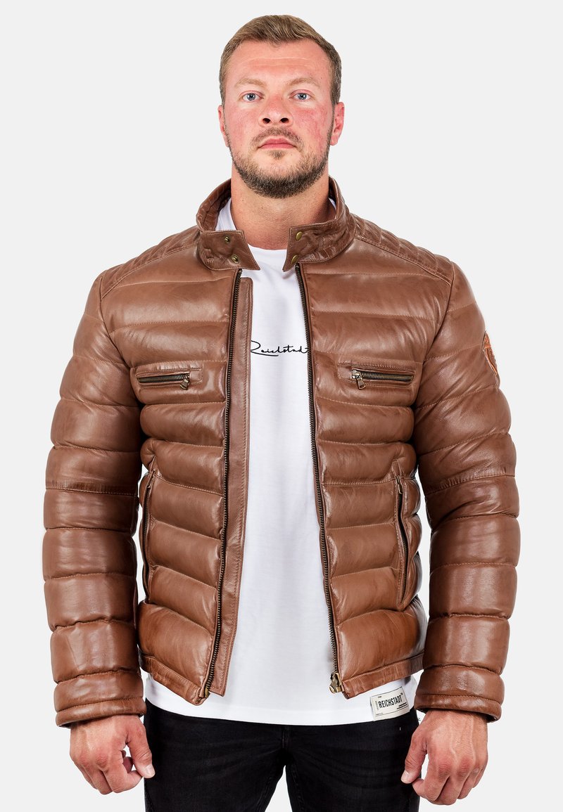 Giacca puffer in pelle marrone con cuciture verticali, tasche con zip e colletto rialzato. Dettaglio con zip in vita e patch con logo.