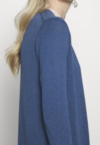 Modrý svetr s texturovaným úpletem, kulatým výstřihem a dlouhými rukávy. Design je jednoduchý, bez dalších vzorů nebo ozdob.