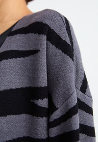 Grå og svart stripete genser med et mykt, teksturert stoff, featuring en v-hals og drop shoulders, fremhever et dristig mønster.