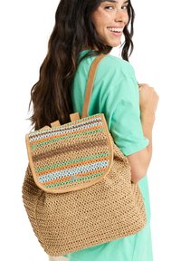 Woven straw backpack with a multicolored striped flap, tan shoulder straps, and a rounded shape. Features a snap closure and textured finish.