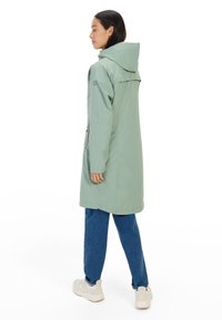 Waterdichte mintgroene parka met een capuchon, lange mouwen, zijzakken en een rechte snit. Gecombineerd met blauwe jeans en lichte sneakers.