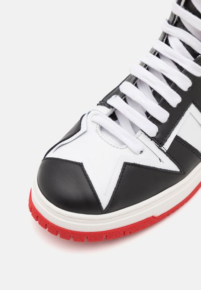 Mustang kõrgpaeltega tennisetossid musta ja valge nahaga, millel on punane kummist tald, tähekujundus varvastes ja valged paelad. Pinna tekstuur on sile.