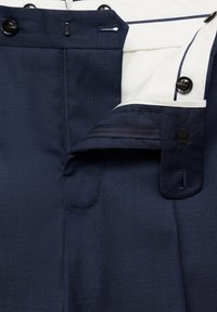 Pantalon habillé bleu marine avec braguette partiellement ouverte, fermeture par bouton et ceinture intérieure blanche avec passepoil foncé.
