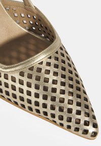 Chaussure à talon haut en métal doré avec un design en treillis découpé, bout pointu et texture en cuir lisse. La semelle et l'intérieur sont de couleur beige.