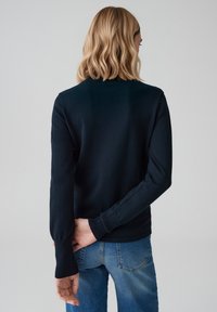 Marineblauwe sweater met lange mouwen van zacht materiaal, met een ronde hals en nauwsluitende manchetten, gecombineerd met lichtblauwe jeans.