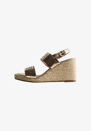 Sandale compensée avec semelle plateforme tissée, deux brides métalliques bronze avec motifs floraux découpés au laser, et boucle de cheville ajustable.