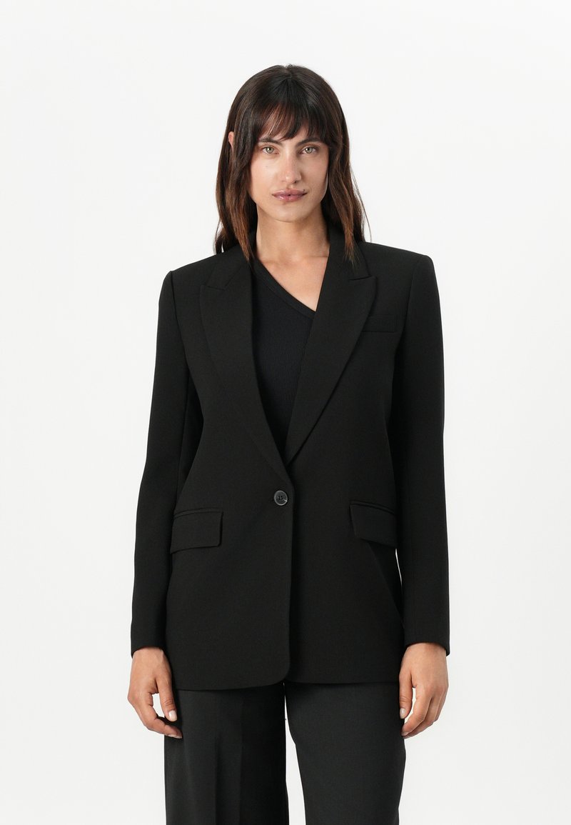 Blazer nera su misura con rever a punta, chiusura con un bottone, due tasche frontali e una texture di tessuto liscia.