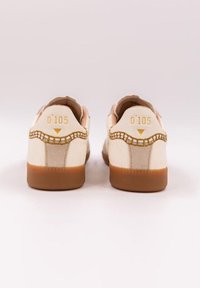 Sneaker bianca con dettagli beige e suola in gomma. Presenta un tessuto testurizzato, cuciture a vista e la dicitura "O'105" impressa sul tallone.
