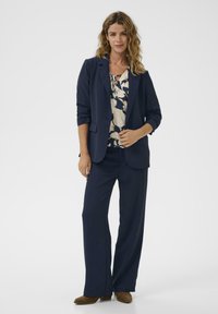 Tengerészkék blézer és bő szárú nadrág összeállítás virágmintás blúzzal, textúrált anyaggal és diszkrét részletekkel. Kényelmes viselet és elegáns megjelenés.