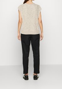 Haut beige en maille avec manches courtes, présentant une finition texturée. Associé à un pantalon noir ajusté et des chaussures noires brillantes.
