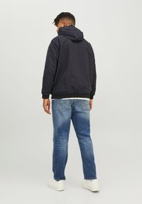 Black hooded jacket with a smooth finish, paired with light blue denim jeans and white sneakers, viewed from the back.