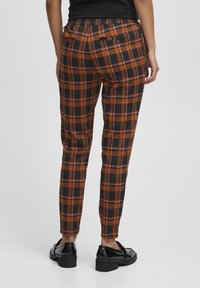 Black and orange plaid trousers with an elastic waist, tapered leg, and two back pockets, worn with shiny black shoes.
