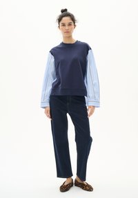 Felpa navy con maniche lunghe a righe blu chiaro, abbinata a pantaloni dritti in denim scuro e scarpe slip-on con stampa animale.