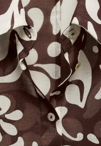 Chemise à boutons marron et crème avec un motif floral, dotée d'un col pointu, de boutons en tissu, et d'une texture douce en lin.