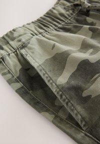 Gros plan sur la ceinture élastique et la poche latérale sur un tissu à motif camouflage vert et gris.