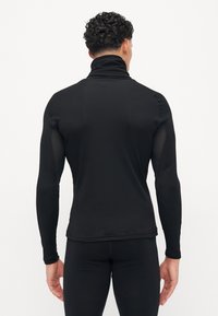 Sort langærmet bluse med høj krave, der har mesh-panels detaljer på siderne, lavet af et glat og strækbart stof.