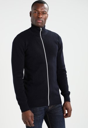 Marineblaue Zip-Pullover mit strukturiertem Zickzackmuster, hohem Kragen und kontrastierendem weißen Reißverschluss. Gerippte Bündchen und Saum; taillierte Passform.