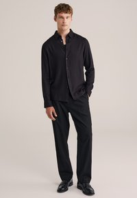 Mustmust valge triibuline särk, millel on peened vertikaalsed triibud, koos mustade pükste ja nahkkingadega. Sile kangas, hästi istuv lõige, lilleline disain.