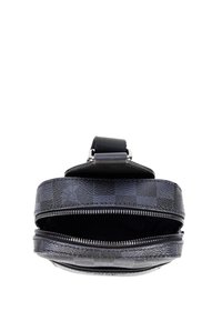 Kulatá černá kožená kabelka se vzorem káro, zapínáním na zip a pevnou horní rukojetí. Vnitřek je podšit tmavou látkou.