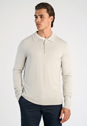 Polo de manga larga en gris claro con cuello con cremallera, fabricado en una tela suave, que presenta puños y dobladillo acanalados. Logo minimalista en el pecho.