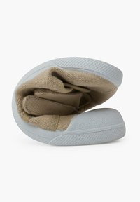 Chaussure en toile beige clair avec une semelle en caoutchouc blanc, présentant un bout rond, un design pliant et une surface texturée.