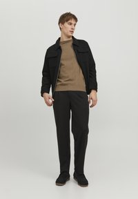 Svart zip-up jakke med to brystlommer, beige strikkegenser, mørke bukser og svarte sko. Minimalistisk design og tettsittende silhuett.