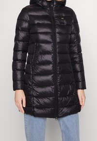 Sort pufferjakke med hætte, der har quiltede sektioner, lynlås lukning og sidelommer. Fremstillet af skinnende, letvægtsmateriale.