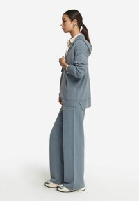 Jasno-niebieska bluza z kapturem i sznurkiem, duże przednie kieszenie, boczne rozcięcia, zestawiona z dopasowanymi spodniami o szerokich nogawkach z miękkiego materiału.