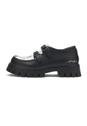 Chaussure en cuir noir et blanc avec double boucle, semelle épaisse à crampons, et inscription décorative sur la zone du talon.