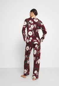 Burgundy floral pajama set features a long-sleeve top and matching pants, adorned with large white and black flowers on a textured fabric.