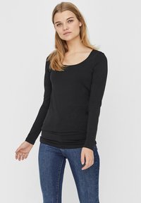T-shirt noir à manches longues avec un col dégagé, fabriqué en tissu doux, design ajusté et texture lisse, associé à un jean bleu.