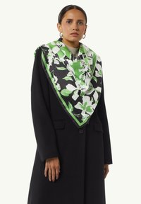 Czarny wełniany płaszcz z dużą zieloną i białą jedwabną chustą w kwiaty. Chusta ma kontrastującą czarną bordiurę oraz charakterystyczne wzory kwiatowe.