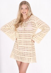 Häkelkleid in Creme, mit einem durchbrochenen Muster mit runden Löchern, Trompetenärmeln und lockerer Passform, geeignet für warmes Wetter.