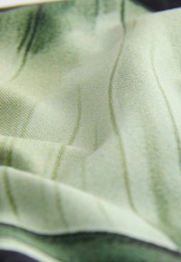 Tekstils, kas ietver gaiši zaļu audumu ar delikātām viļņveida līnijām un mīkstu tekstūru, salikts krokās, ar nelielu spīdumu.