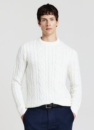 Maglione bianco a trecce con scollo rotondo e polsini a costine, indossato sopra pantaloni blu navy. Presenta un motivo testurizzato su tutta la superficie.