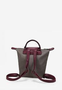 Mochila de nailon gris con acentos de cuero burdeos, que cuenta con dos asas superiores, correas ajustables para los hombros y un cierre de cremallera.