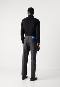Haut noir à manches longues, jean en denim gris avec une étiquette bleue "HUGO" à l'arrière, et chaussures noires. Texture lisse et coupe décontractée.
