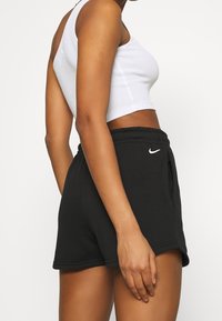 Svarta bomullsidrottsbyxor med dragsko i midjan, fickor på sidorna och en liten vit Nike-logotyp på vänster framsida.