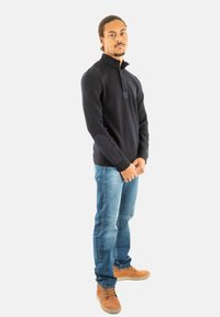 Maglione zip-up navy con colletto alto, abbinato a jeans azzurri chiari e stivali color sabbia. Il maglione presenta dettagli in tessuto contrastante sulle maniche.