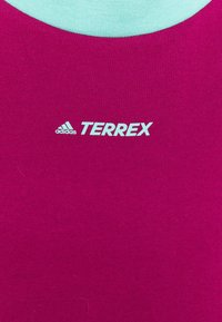 Fuchsia Sportshirt mit glatter Textur, versehen mit hellblauen Akzenten und dem "adidas TERREX" Logo in einer kontrastierenden Farbe.