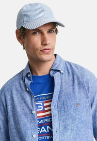 Blauw-wit gestreepte pet, stoffen overhemd in lichtblauw, graphic blauw T-shirt met rode en witte accenten, met een merklogo.