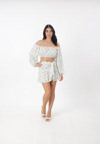 Weißes Blumenträgershirt mit Puffärmel und passendem Wickelrock, der ein Bindedetail aufweist. Der Stoff hat eine weiche Textur und ein kleines Blumenmuster.