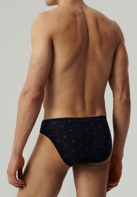 Granatowe majtki typu slip z małym, powtarzającym się wzorem geometrycznym. Wykonane z miękkiej tkaniny, z wygodnym elastycznym pasem. Klasyczny krój slipów.