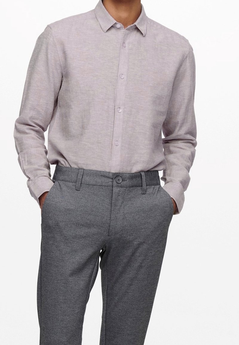 Camisa de botones de manga larga color púrpura claro con un acabado texturizado, combinada con pantalones grises a medida con cierre de botón y bolsillos laterales.